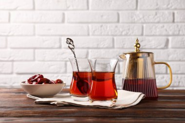 Cam bardaklarda lezzetli Türk çayı, beyaz tuğla duvara karşı ahşap masada hurma ve çaydanlık.