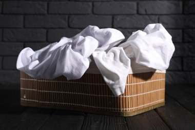 Siyah ahşap yüzeyde çamaşır sepeti dolusu giysiler.