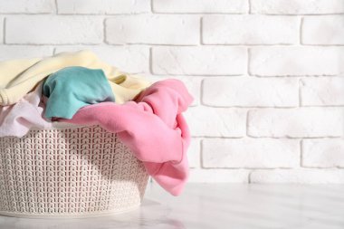 Çamaşır sepeti beyaz mermer yüzeyde kıyafetlerle dolu. Metin için boşluk