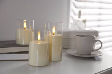 Decorative LED candles, tea, books and tissues on white table indoors, closeup
