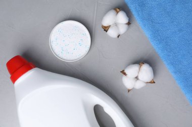 Bir şişe yumuşatıcı, çamaşır tozu, havlu ve pamuk çiçekleri gri masada, düz yerde.