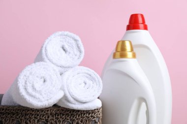 Kumaş yumuşatıcı şişeleri ve pembe arka planda rulo havlular, yakın plan.