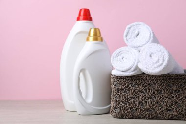 Kumaş yumuşatıcı şişeler ve ahşap masaya sarılmış havlular. Pembe arka plana karşı, yakın plan. Metin için boşluk