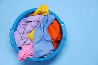 Plastic basin with clothes on light blue background, top view
