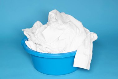 Açık mavi arka planda çamaşırları olan plastik leğen, yakın plan.