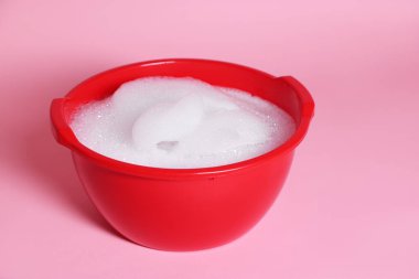 Pembe arka planda sabunlu kırmızı plastik leğen, yakın plan.