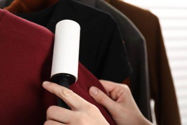 Woman cleaning sweater with lint roller at home, closeup