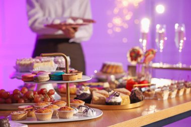 Different delicious desserts on buffet table and waiter, selective focus