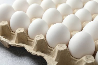 Yumurta kutusunda çiğ tavuk yumurtası. Gri masada, yakın plan.