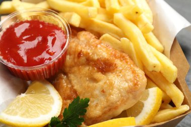 İngiliz Geleneksel Balık ve patates kızartması soslu, limonlu ve maydanozlu kağıt kutuda, yakın plan.