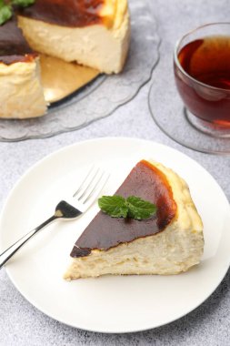 Piece of delicious Basque cheesecake with mint and tea on light grey table, closeup