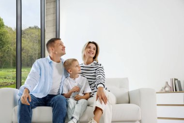 Klimalı uzaktan kumandalı küçük bir çocuk ve ailesi evdeki kanepede.