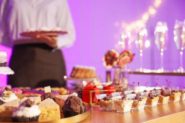 Different delicious desserts on buffet table and waiter, selective focus