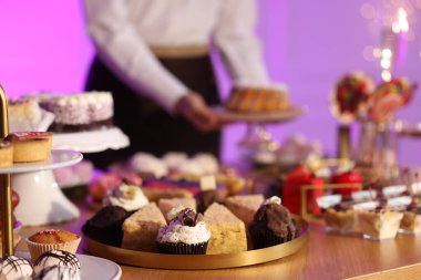 Different delicious desserts on buffet table and waiter, selective focus