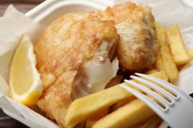 İngiliz Geleneksel Balık ve patates kızartması. Paket servis kutusunda limon var. Yakın plan.
