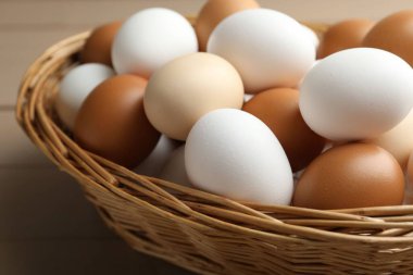 Many raw chicken eggs in wicker basket on wooden table, closeup