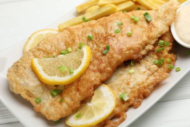 Beyaz ahşap masada soslu, limonlu ve yeşil soğanlı İngiliz Geleneksel Balık ve patates kızartması.