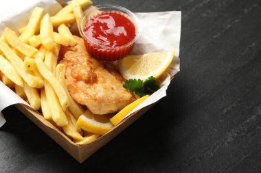 Sos, limon ve maydanozlu İngiliz Geleneksel Balık ve patates kızartması siyah desenli masada, yakın plan.