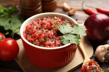 Delicious salsa sauce in bowl and ingredients on wooden table, closeup