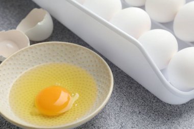 Bir sürü çiğ tavuk yumurtası ve bir tanesi gri masada kırılmış, yakın plan.