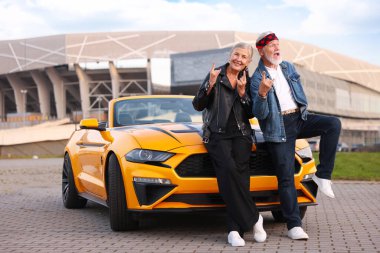 Modern Cabriolet yakınlarındaki şık yaşlı çift açık havada kaya jesti sergiliyor.