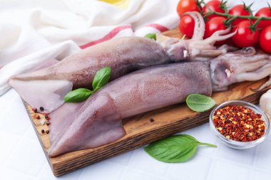 Fresh raw squids, tomatoes and spices on white tiled table, closeup