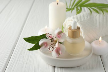 Beautiful spa composition with essential oil and burning candles on white wooden table, closeup. Space for text