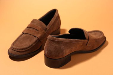 Soluk turuncu arka planda bir çift şık kahverengi ayakkabı, yakın plan.