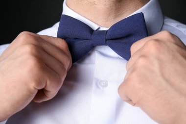 Takım elbiseli adam papyonunu siyah arka planda ayarlıyor.