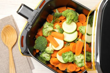 Beyaz ahşap masada çiğ havuç, brokoli ve kabak kızartma makinesi.