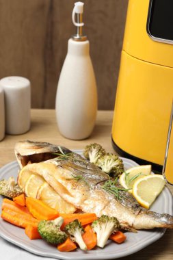 Pişmiş balık, biberiye, limon, sebze ve tava ahşap masada, yakın plan.