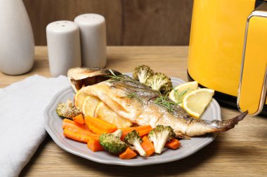 Pişmiş balık, biberiye, limon, sebze ve tava ahşap masada, yakın plan.