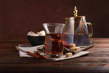 Cam bardakta lezzetli Türk çayı, kahverengi şeker, tarçın, tatlı ve çaydanlık ahşap masada renk arka planına karşı, yakın plan