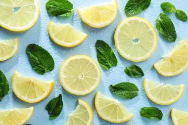 Limon dilimleri, nane ve su damlaları açık mavi arka planda, düz yerde