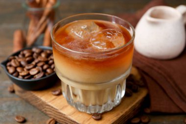 Tasty iced coffee with milk and beans on wooden table, closeup