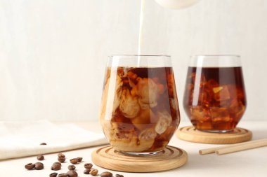 Beyaz masada buzlu kahve bardağına süt dökerek.