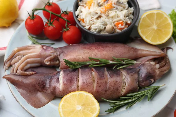 Çiğ mürekkep balıkları, dolma, biberiye, limon ve domatesler beyaz fayanslı masada, yakın plan.