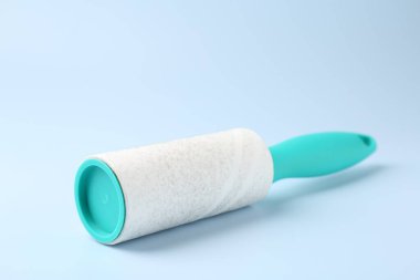 Lint roller with used sticky tape on light blue background, closeup