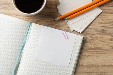Boş notlar, defter, bir fincan kahve ve tahta masa üzerindeki kalemler, düz yatak. Metin için boşluk