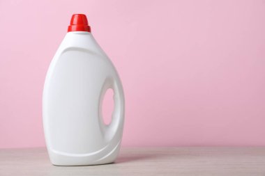 Ahşap masada pembe arkaplana karşı yumuşatıcı şişesi, metin için boşluk