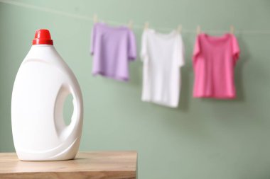 Ahşap masada bir şişe yumuşatıcı ve soluk tozlu yeşil arka planda asılı giysiler, metin için yer