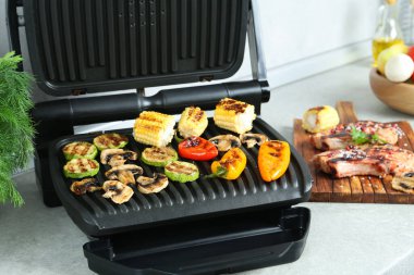 Mutfaktaki ışık masasında nefis sebzeler ve bifteklerle elektrikli ızgara. Yakın plan.