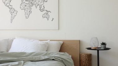 Yatak odasındaki beyaz duvarın yanında çarşafları, sehpası ve lambası olan rahat geniş bir yatak, sola hareket eden kamera.