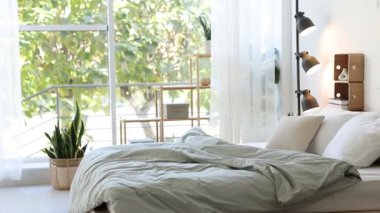 Yatak odasındaki beyaz duvarın yanında çarşaflı, sehpalı, sandalyeli ve lambalı rahat büyük bir yatak.