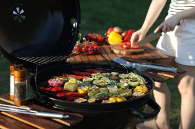 Vejetaryen barbeküsü. Dışarıdaki masada ürünleri kesen kadın, pişmiş sebzelerle ızgaraya odaklan.