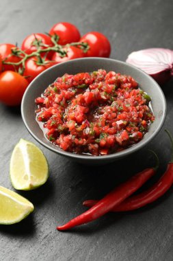 Delicious salsa sauce in bowl and ingredients on dark grey table, closeup