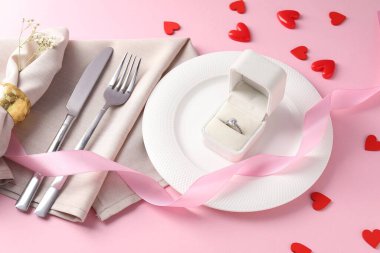 Romantik yemek için güzel bir masa ve pembe arka planda nişan yüzüğü olan bir kutu.
