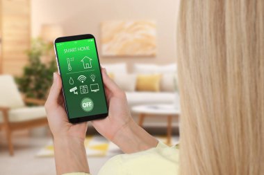Woman using smart home app on mobile phone to control house features, closeup