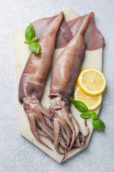 Çiğ mürekkep balıkları, limon ve fesleğen açık gri masa, üst manzara.