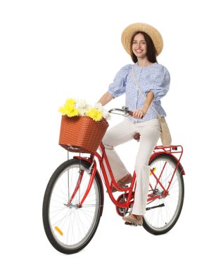 Şapkalı gülümseyen kadın beyaz arka planda bir sepet çiçekle bisiklet sürüyor.